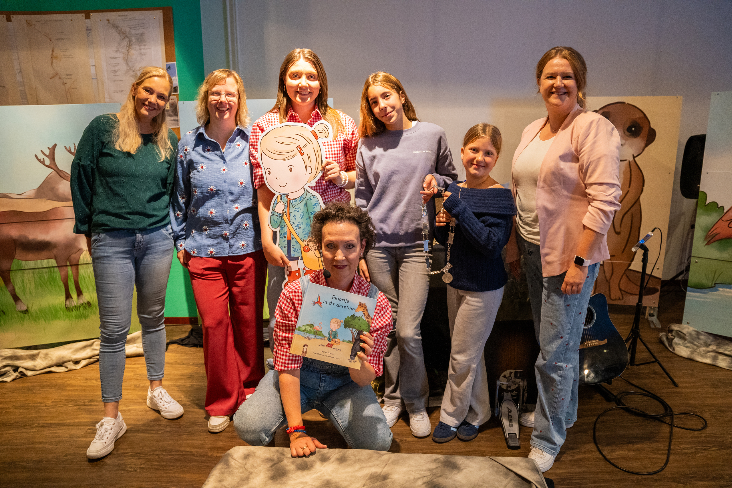 Groepsfoto van schrijfster Astrid Frush en illustrator Melanie Frissen van het boek "Floortje in d'r deretuin", samen met Myrthe en Peggy Alofs van Goud Verteltheater, locokinderburgemeesters Jaelinn Janssen en Livia Notten en wethouder Merle Brüning